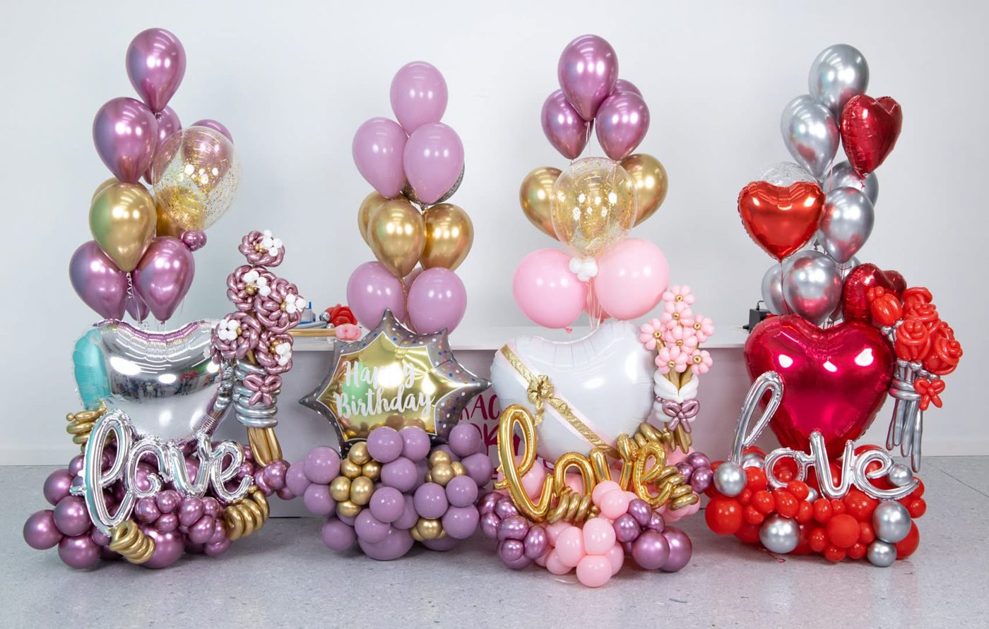 Row of pink, gold and red balloon arrangements with script signs